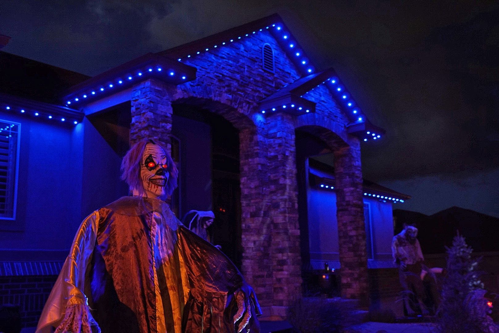 A skeleton is standing in front of a house with blue lights.