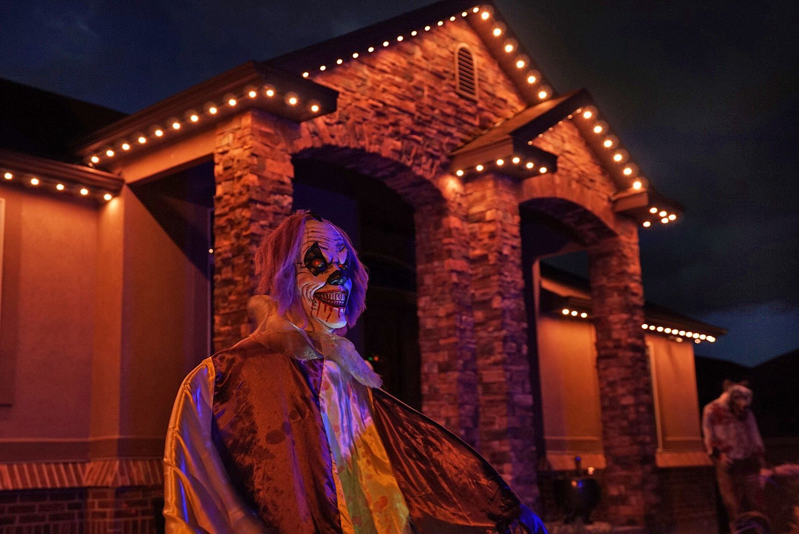 A scary clown is standing in front of a house at night.