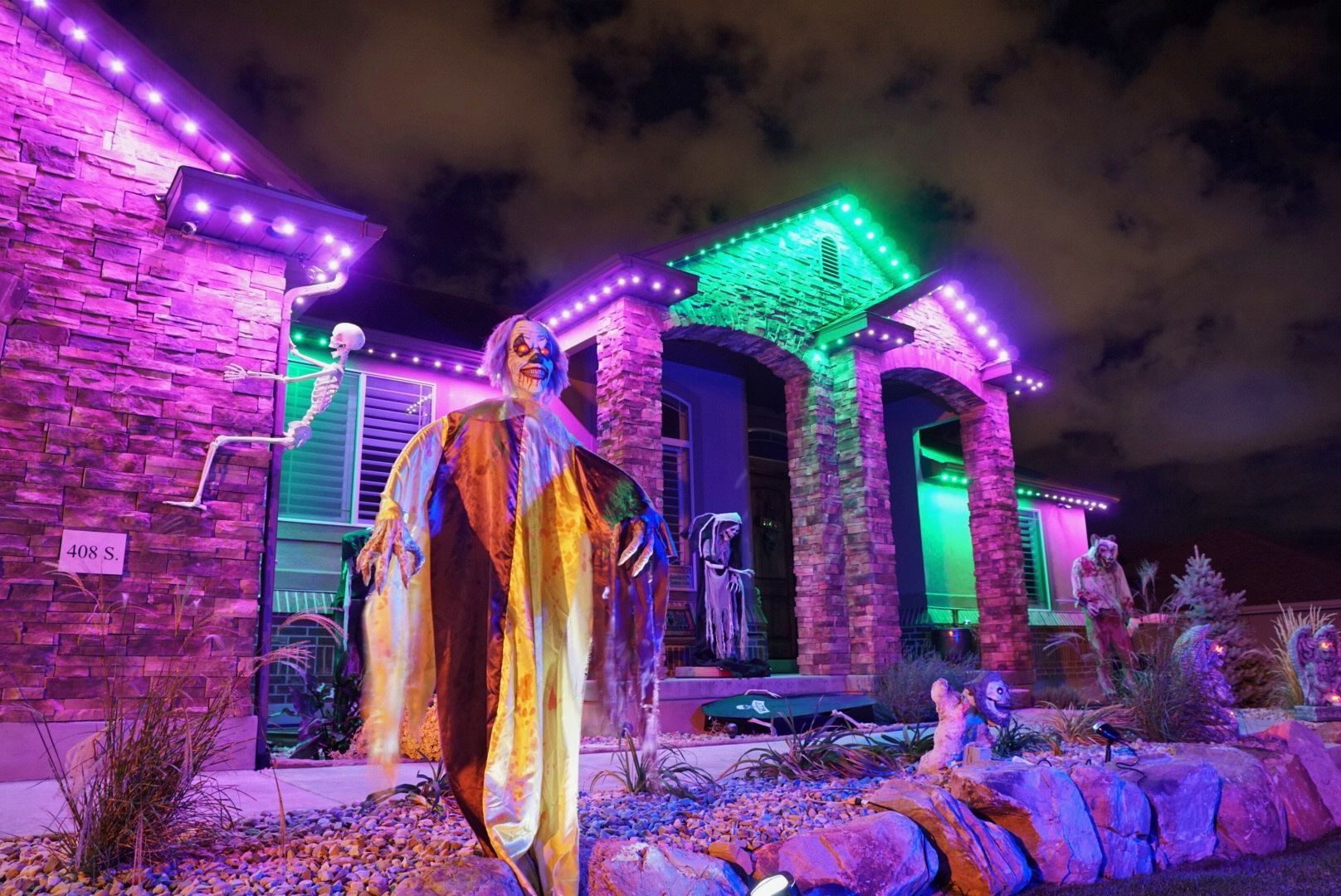 A house decorated for halloween with purple and green lights and a skeleton.