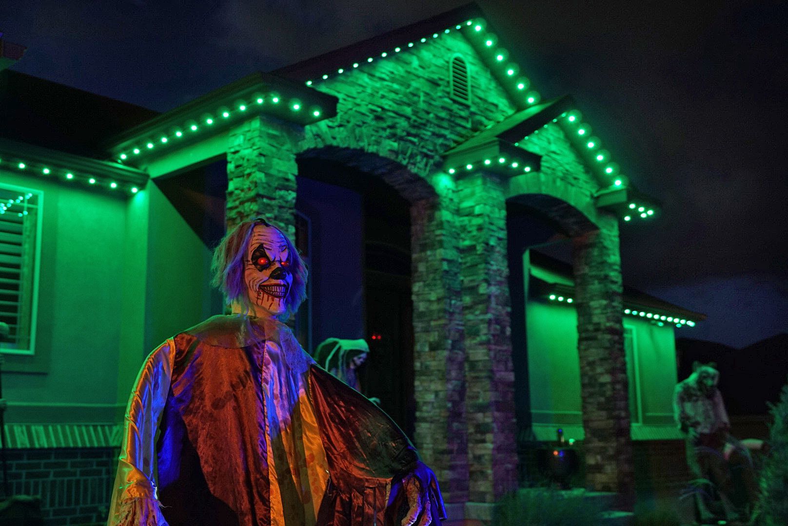 A skeleton is standing in front of a house with green lights.