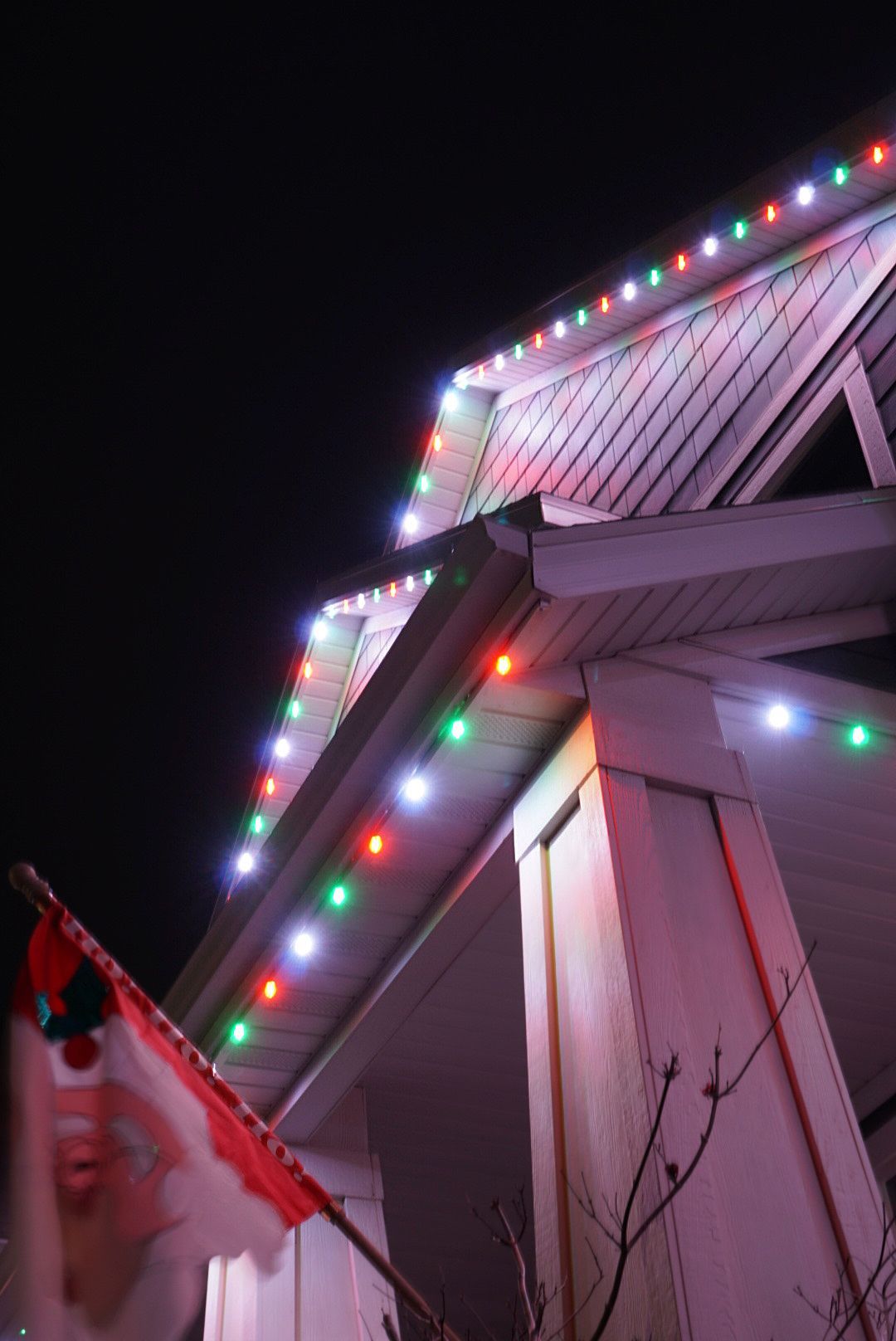 A canadian flag is flying in front of a house decorated with christmas lights.