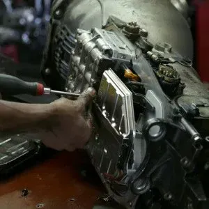 Mechanic using a screwdriver to work on a car transmission.