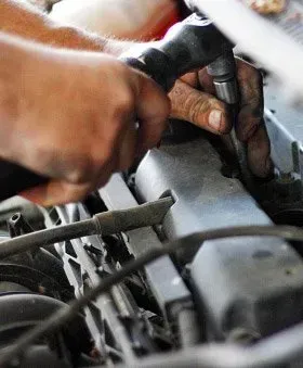 Mechanic working on a car engine with a wrench, hands covered in grease.