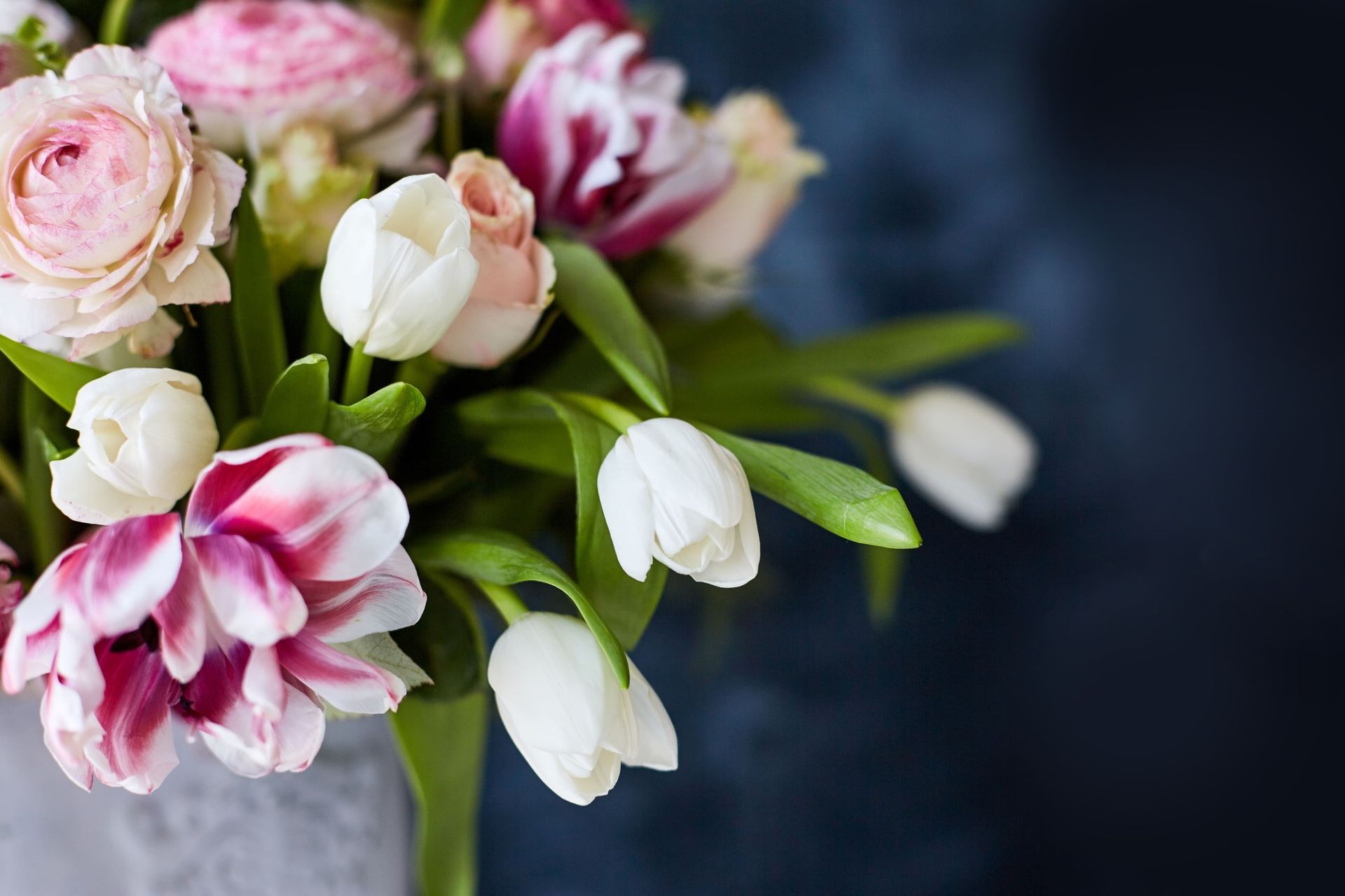 Bouquet of pink and white flowers, including tulips and roses, against a dark blue background.