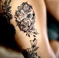 A woman has a tattoo of a skull and roses on her thigh.
