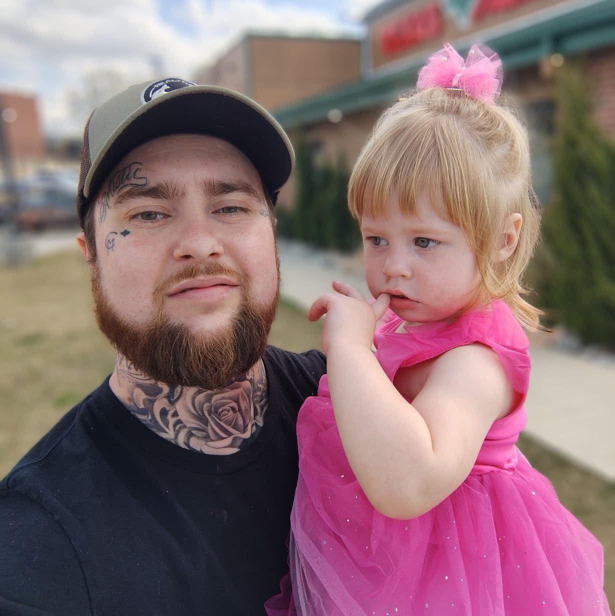 A man with a beard is holding a little girl in a pink dress.