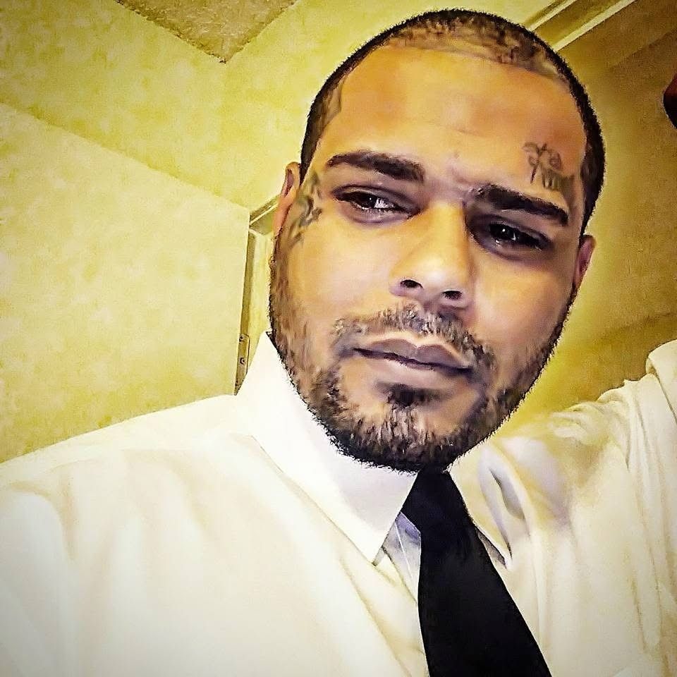 A man with a tattoo on his forehead is wearing a white shirt and black tie