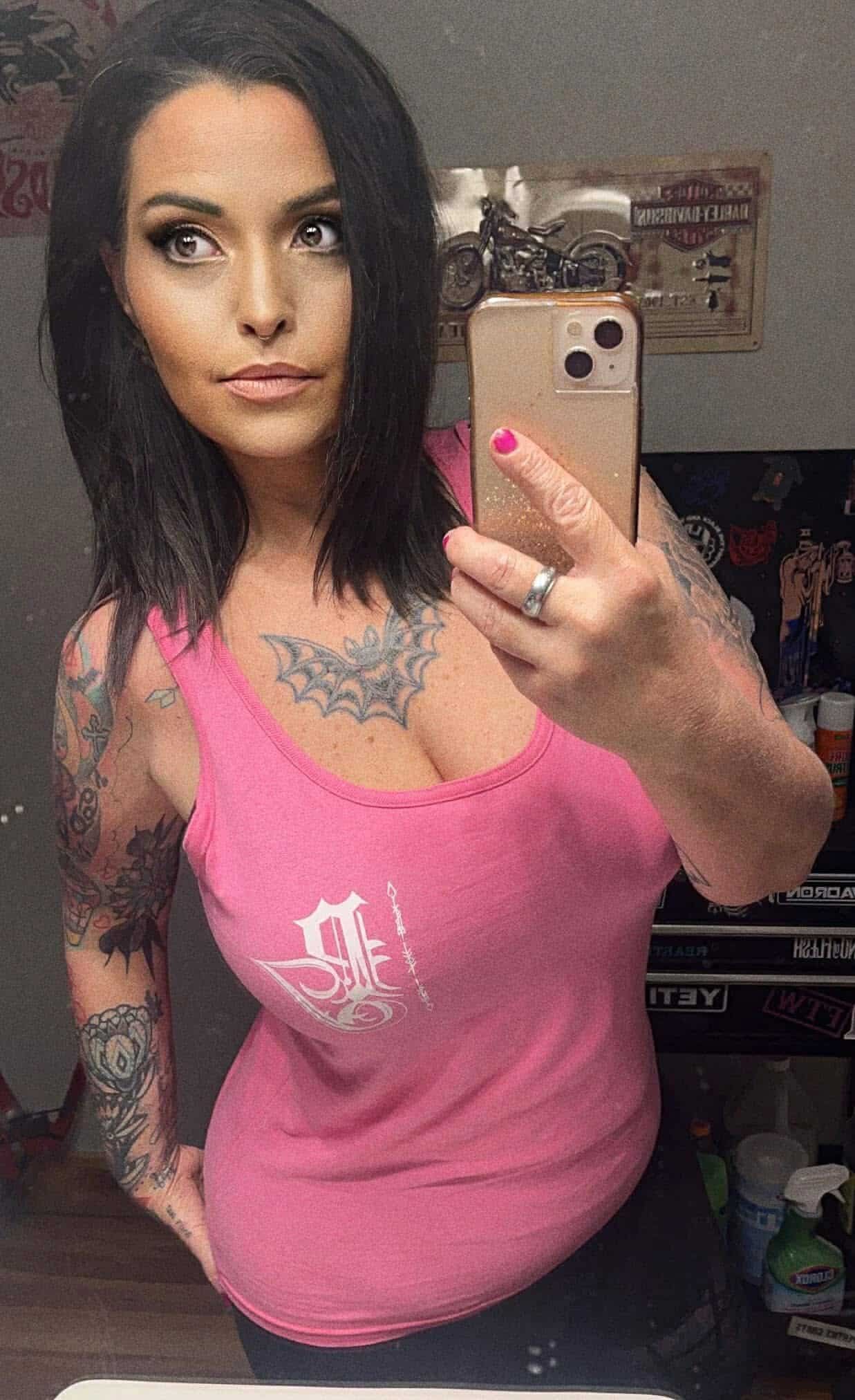 A woman in a pink tank top is taking a selfie in front of a mirror.