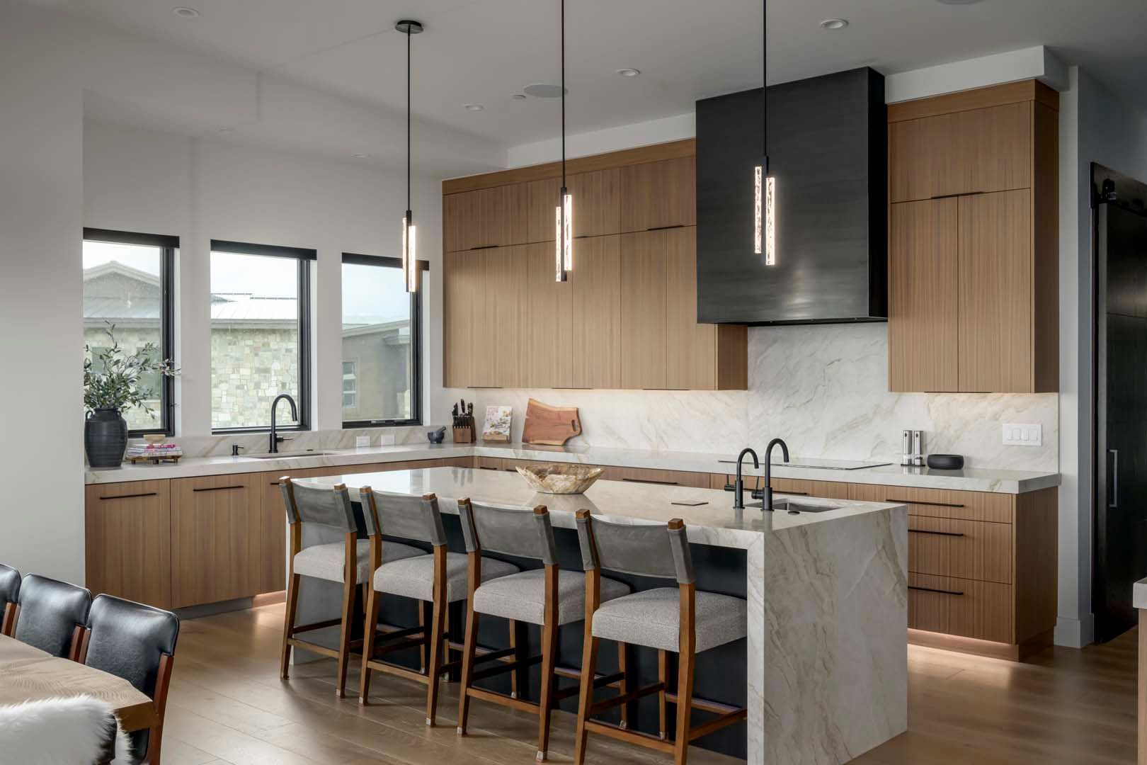 Modern kitchen with light wood cabinets, marble countertops, island with seating, and dark range hood.