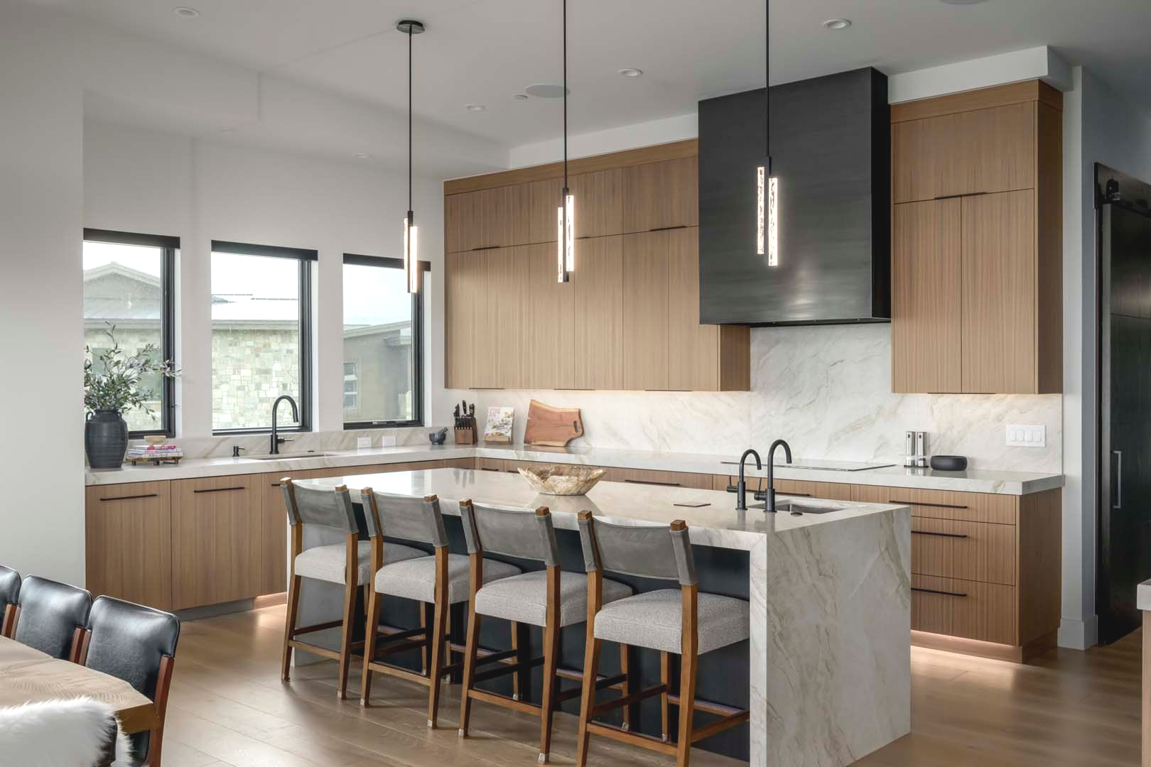 Modern kitchen with light wood cabinets, marble countertops, and island with bar stools.