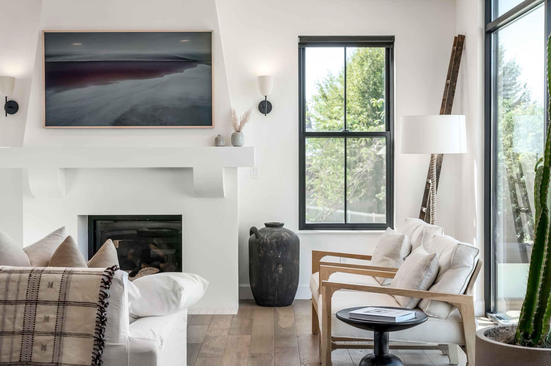Living room with white fireplace, large window, neutral furniture, and modern decor.