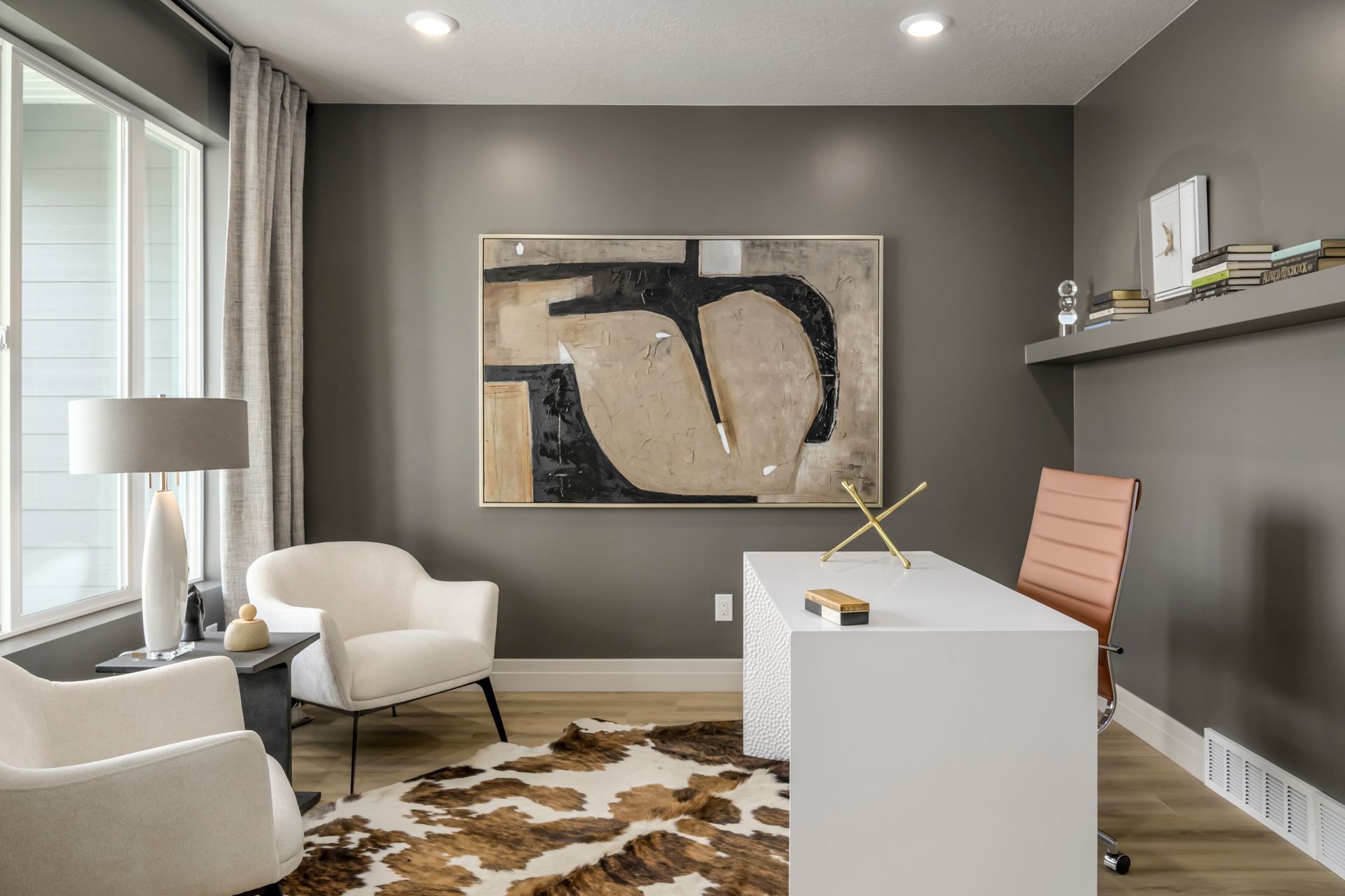 Home office with white desk, abstract art, two chairs, rug, and pink office chair.