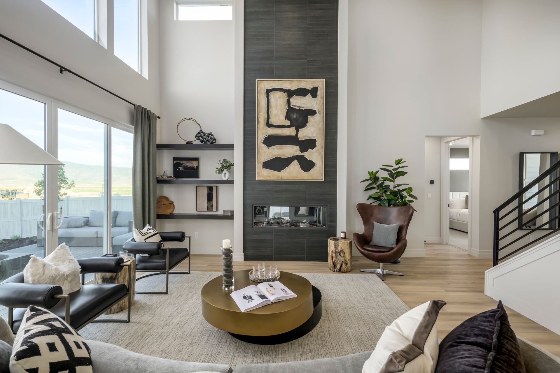 Modern living room with fireplace, abstract art, seating, and large windows with outdoor view.