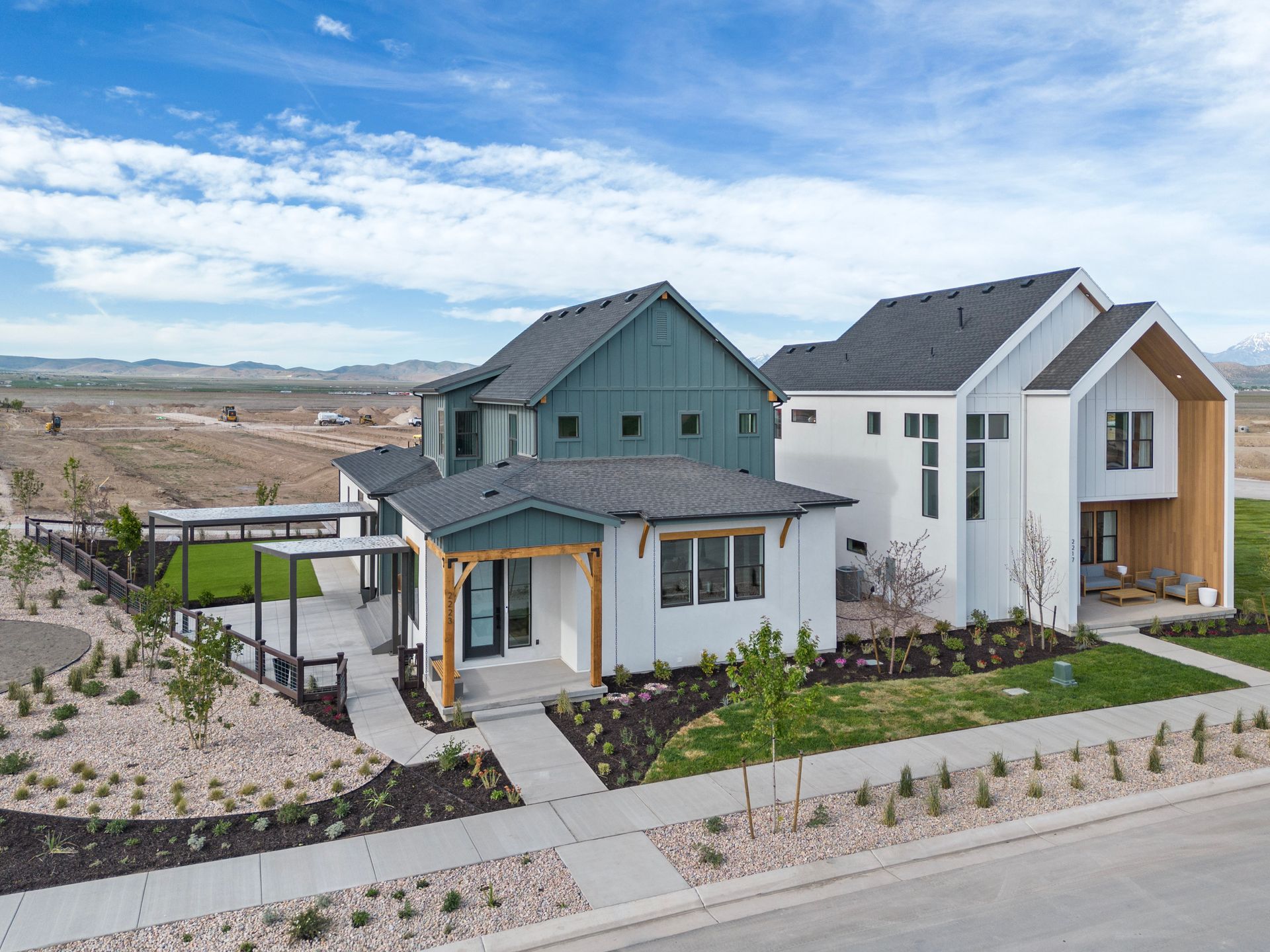 Modern homes with dark and light exteriors, set against a backdrop of a vast plain and blue sky.