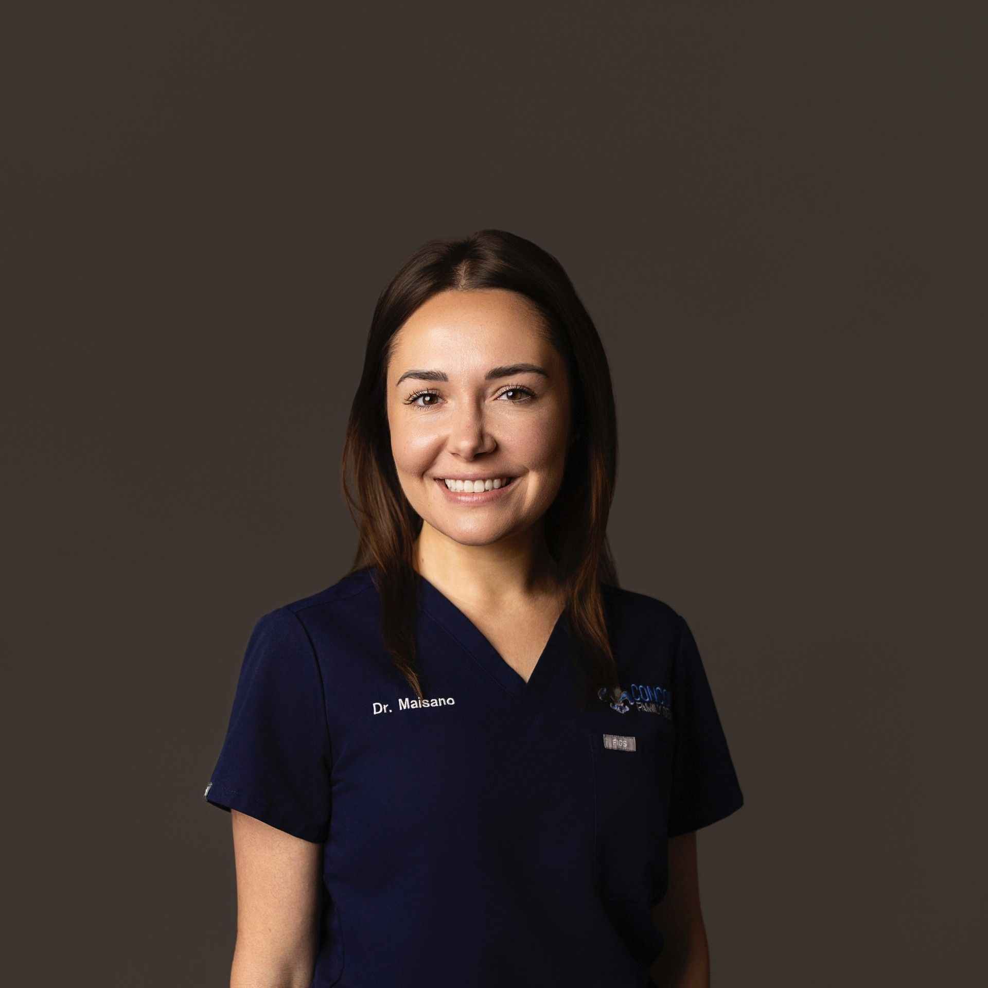 Smiling woman wearing a navy blue scrub top with a name badge.