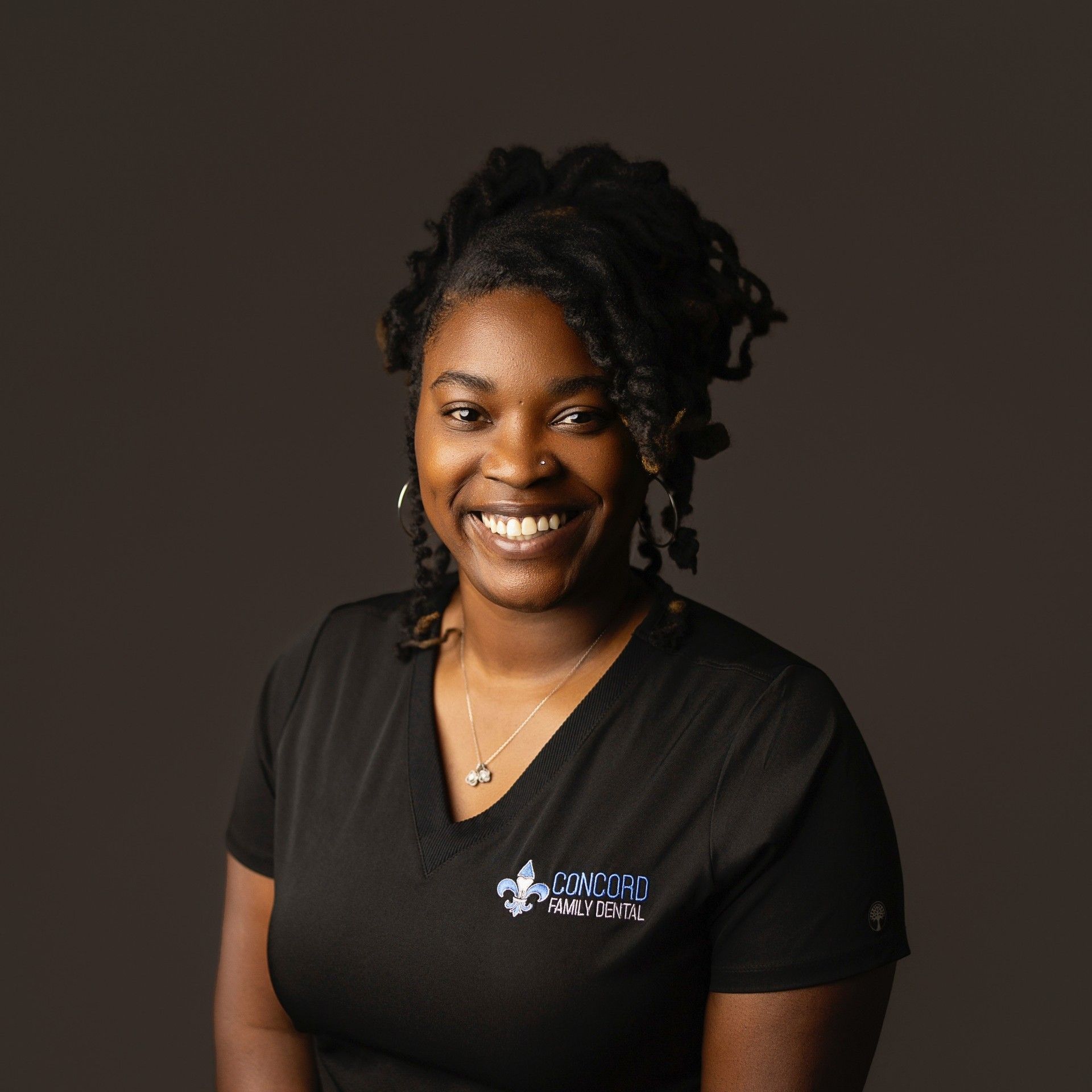 Black woman with locs smiling, wearing a black shirt with a logo.