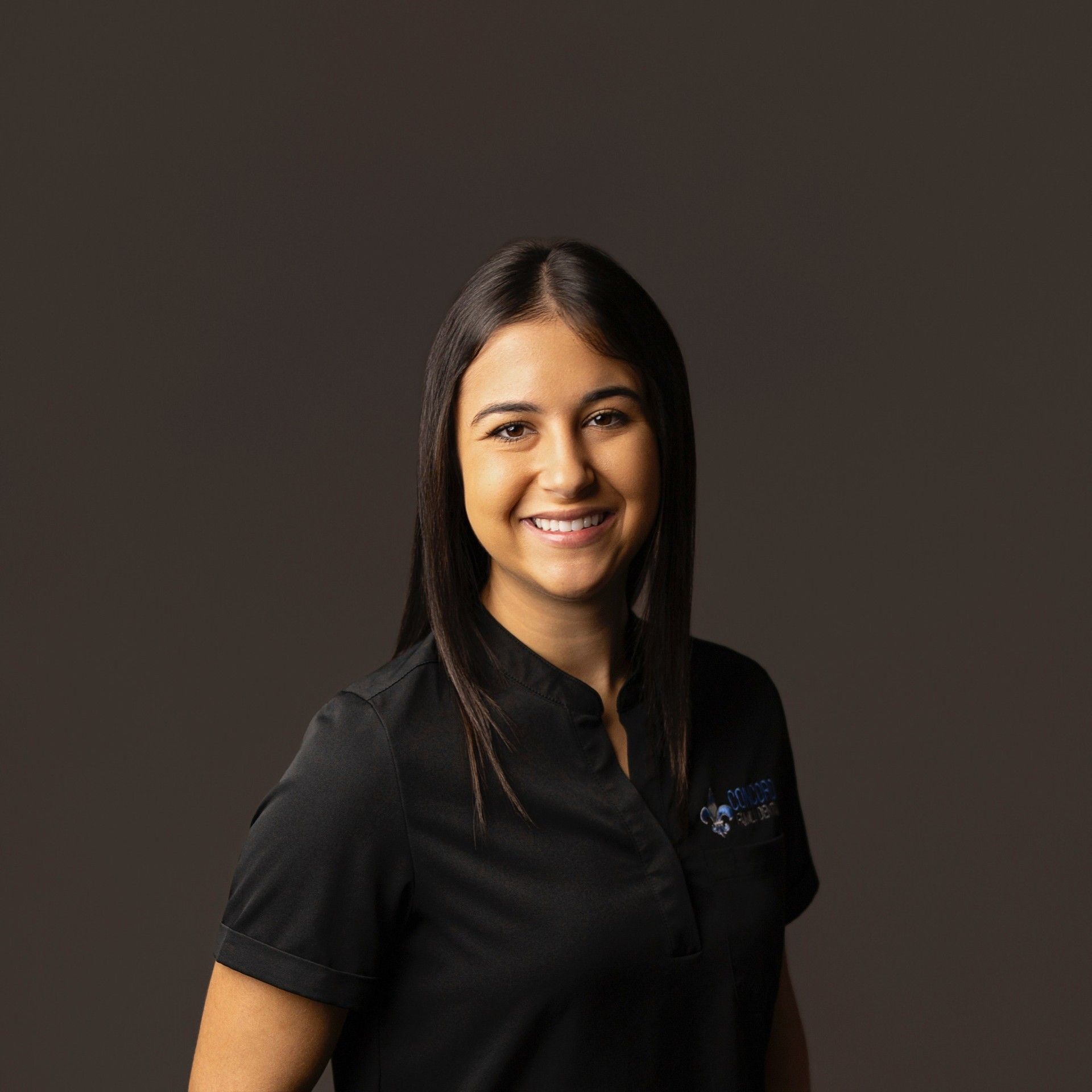 Woman with long dark hair and a friendly smile, wearing a black collared shirt.