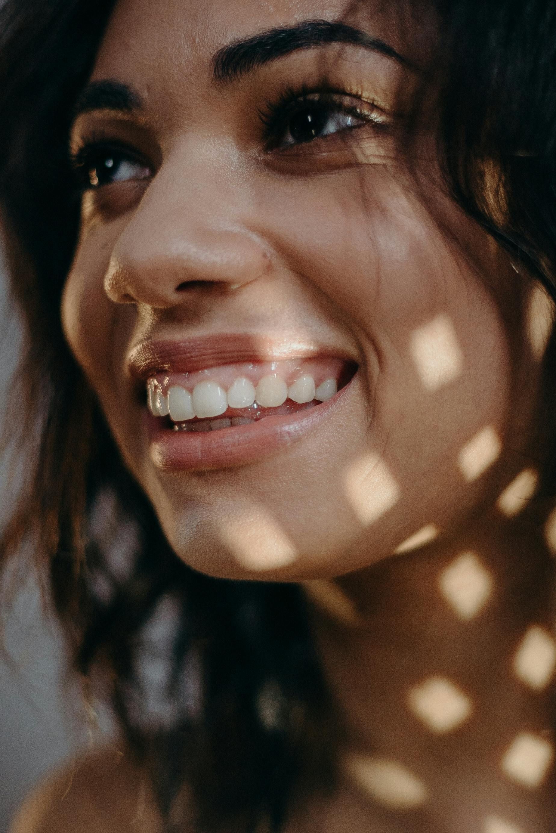 A close up of a woman 's face smiling with the sun shining on her face.