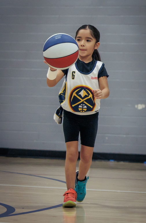 Youth basketball player dribbling a red, white and blue basketball while wearing a Denver Nuggets jersey.