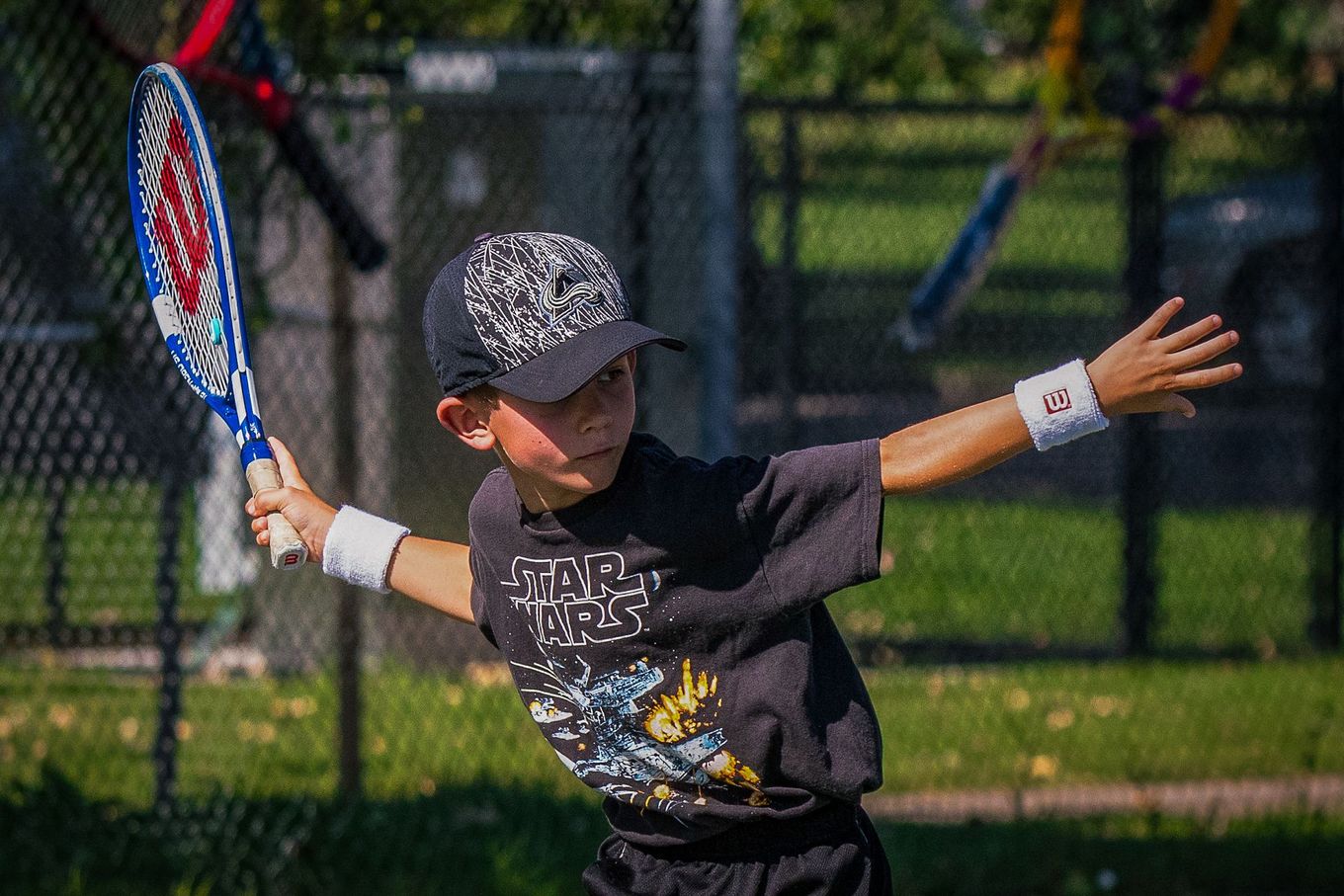 Youth tennis player in black shirt preparing to swing the raquet.