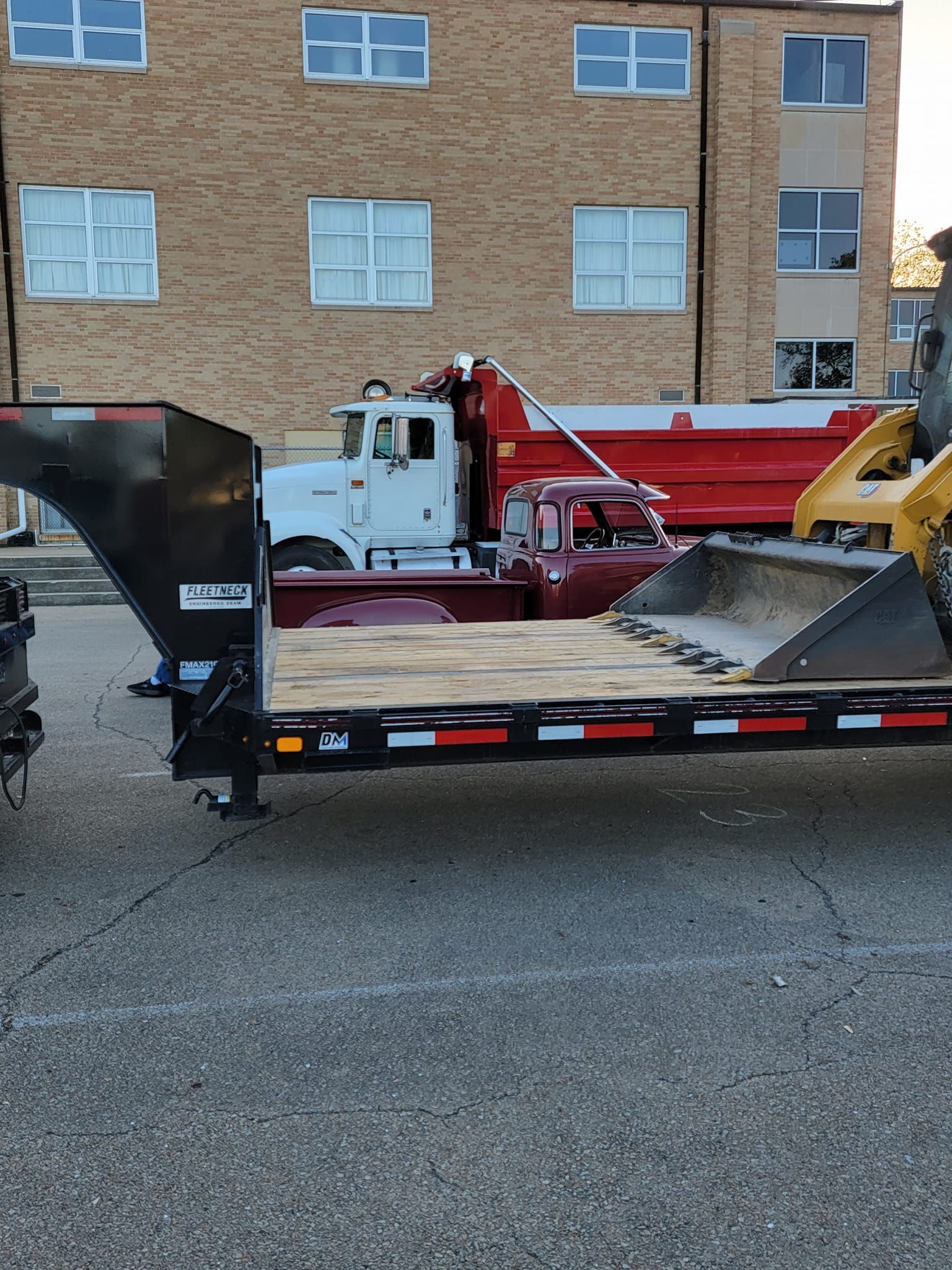 A trailer with a bulldozer on it is parked in front of a brick building.