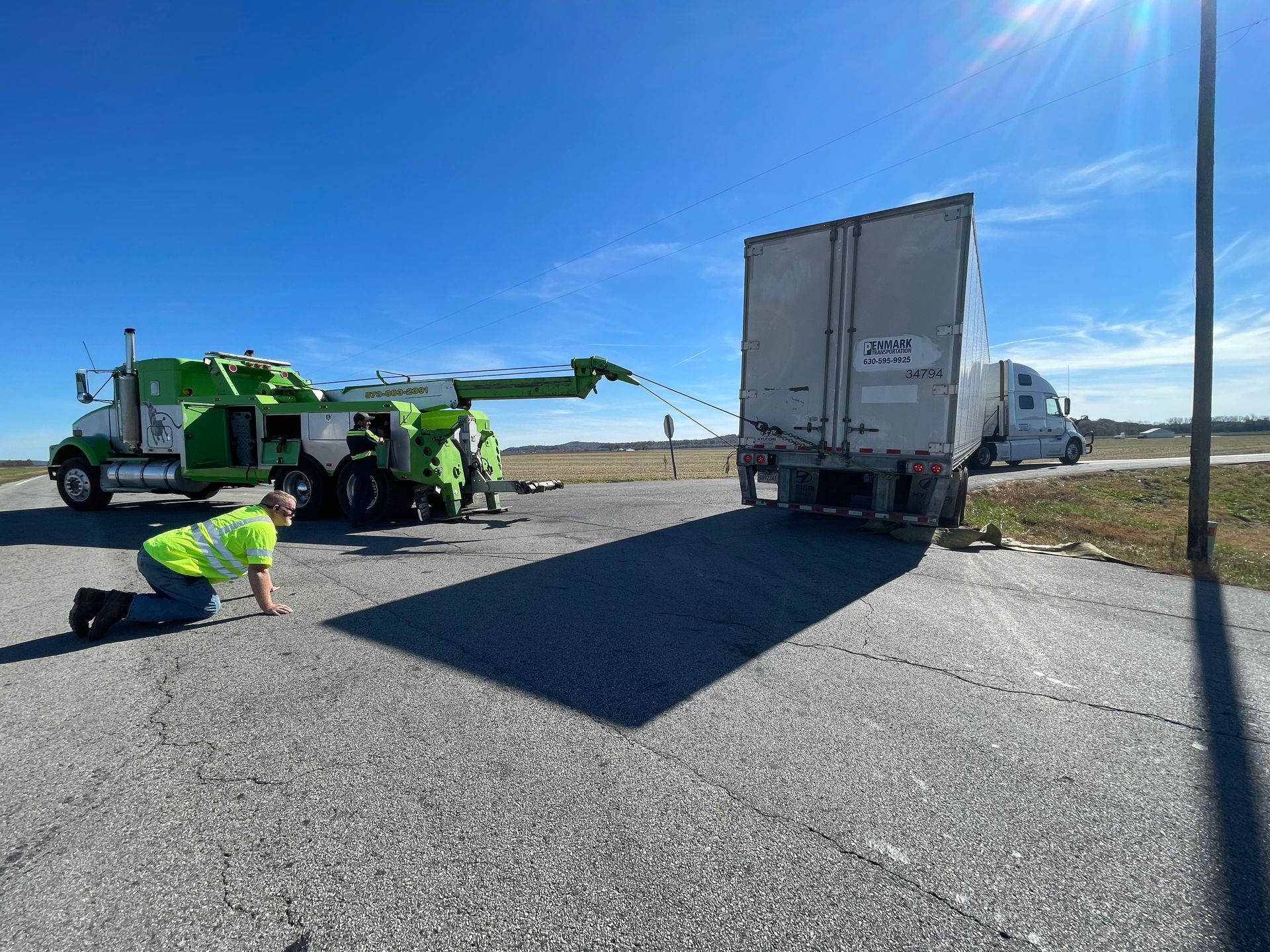 A tow truck is towing a semi truck on the side of the road.
