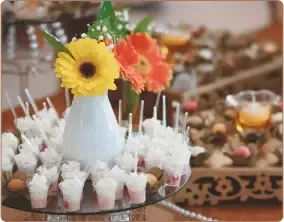 A table featuring a glass serving stand with white dessert cups and a vase with yellow and orange flowers.