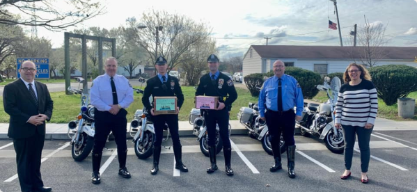 A line of six people standing in a parking lot, four in uniforms and two in civilian attire, holding plaques and gifts.