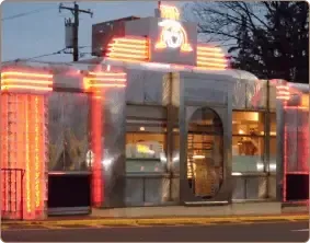 A stainless steel retro-style diner with glowing orange neon accents along its exterior walls at dusk.
