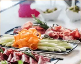 A spread of gourmet appetizers on a white table, including thinly sliced cured meats, melon strips, and small bowls.