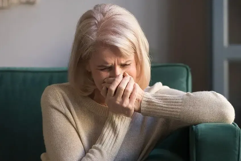 A person sitting on a green couch, shielding their face with their hands while looking distressed.