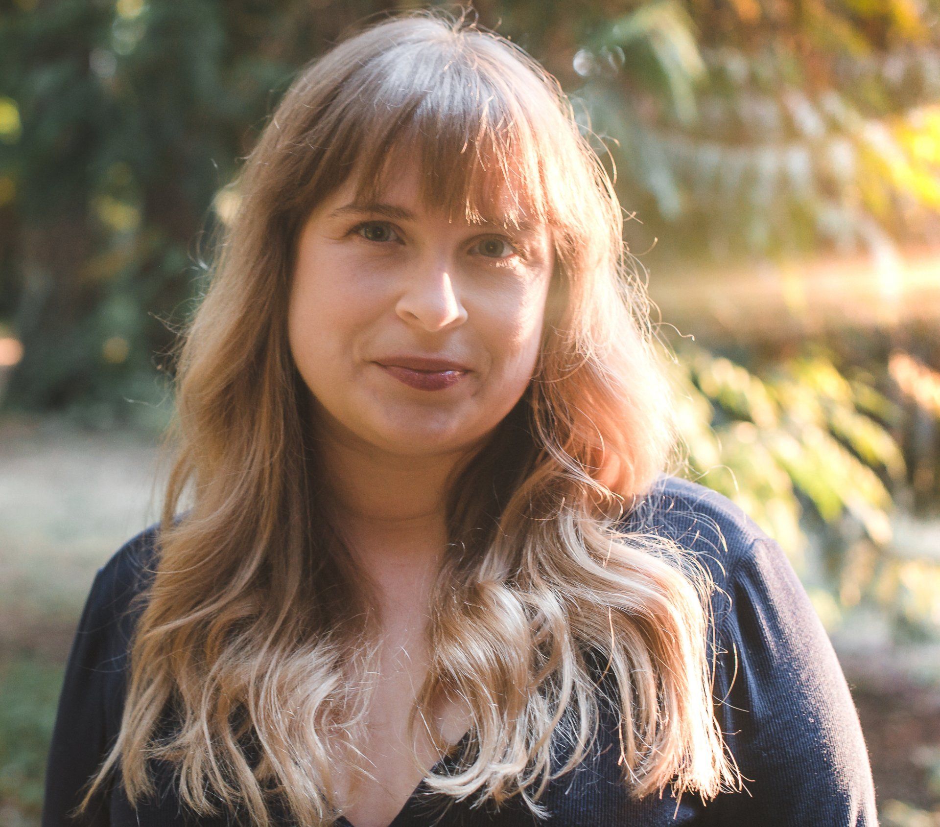 Sarah McBee standing in the woods with sun shining on her face.