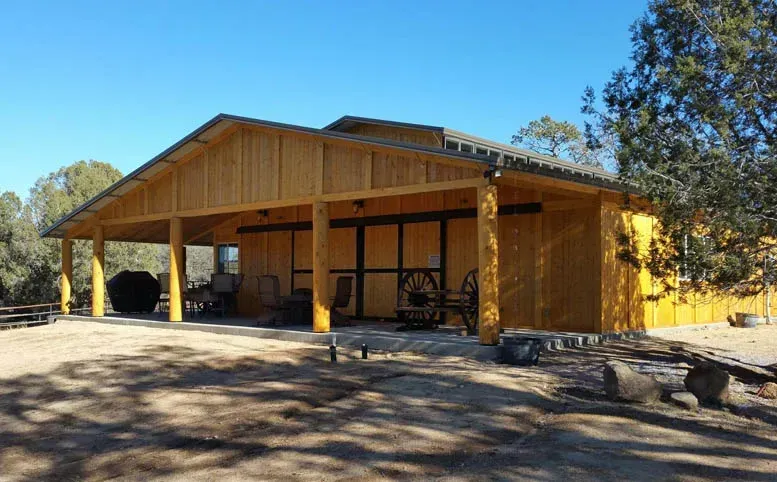 A large wooden building with a covered porch in the middle of a field.