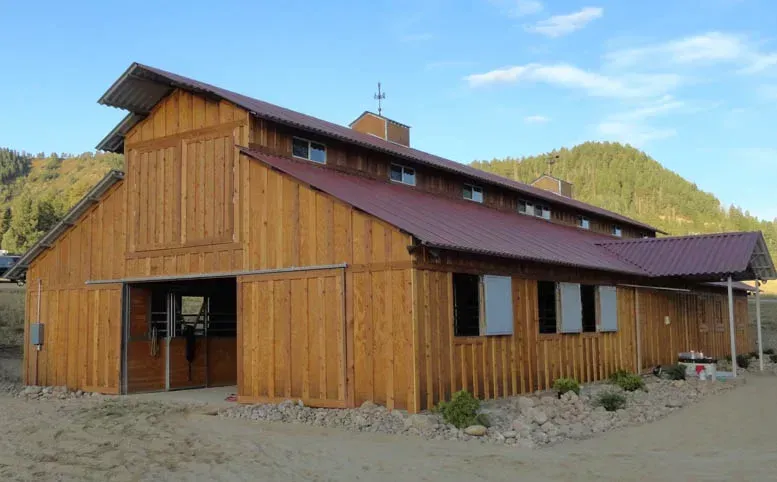 A large wooden barn with a red roof and mountains in the background.
