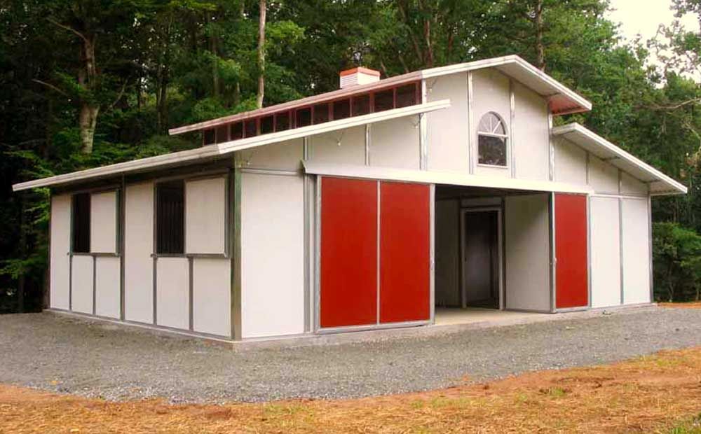A white barn with red sliding doors is surrounded by trees