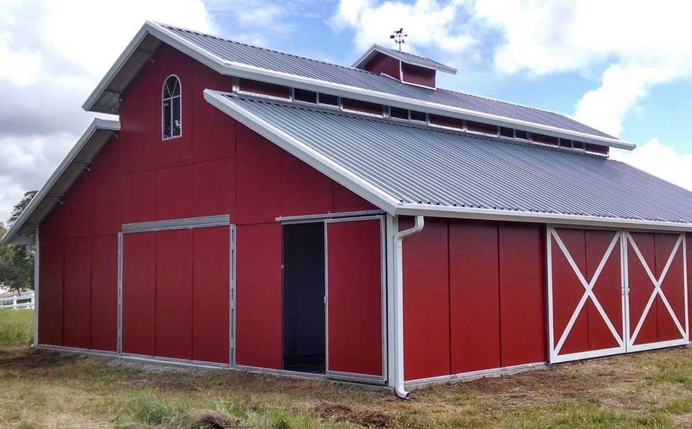 A large red barn with a gray roof is sitting in the middle of a grassy field.