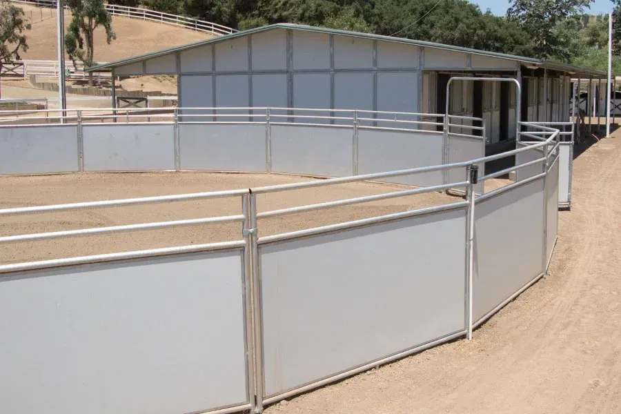 A white fence surrounds a dirt field in front of a building.