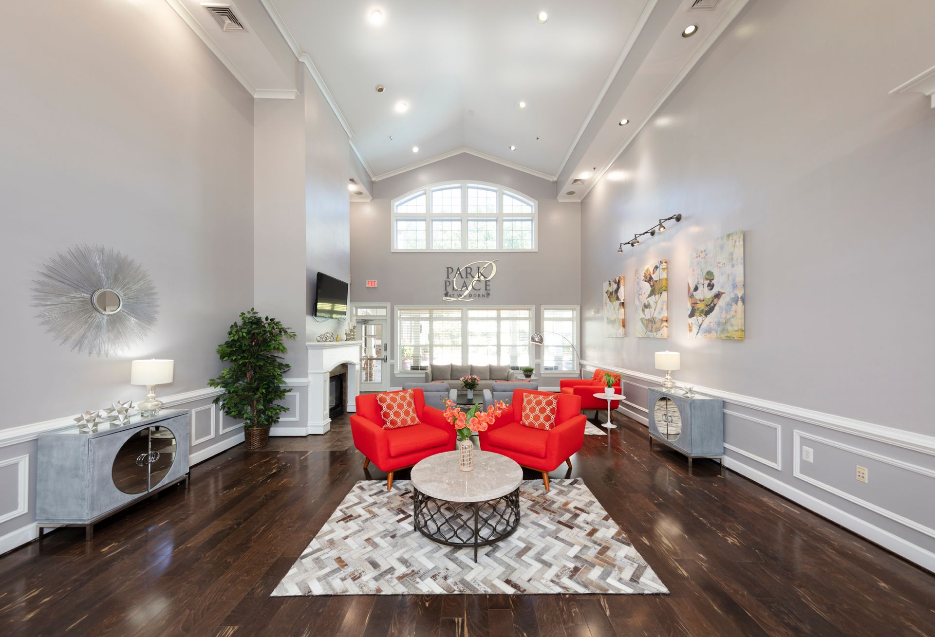 Spacious gray-walled lobby with red chairs, a coffee table, and decorative cabinets. A large window at the far end.