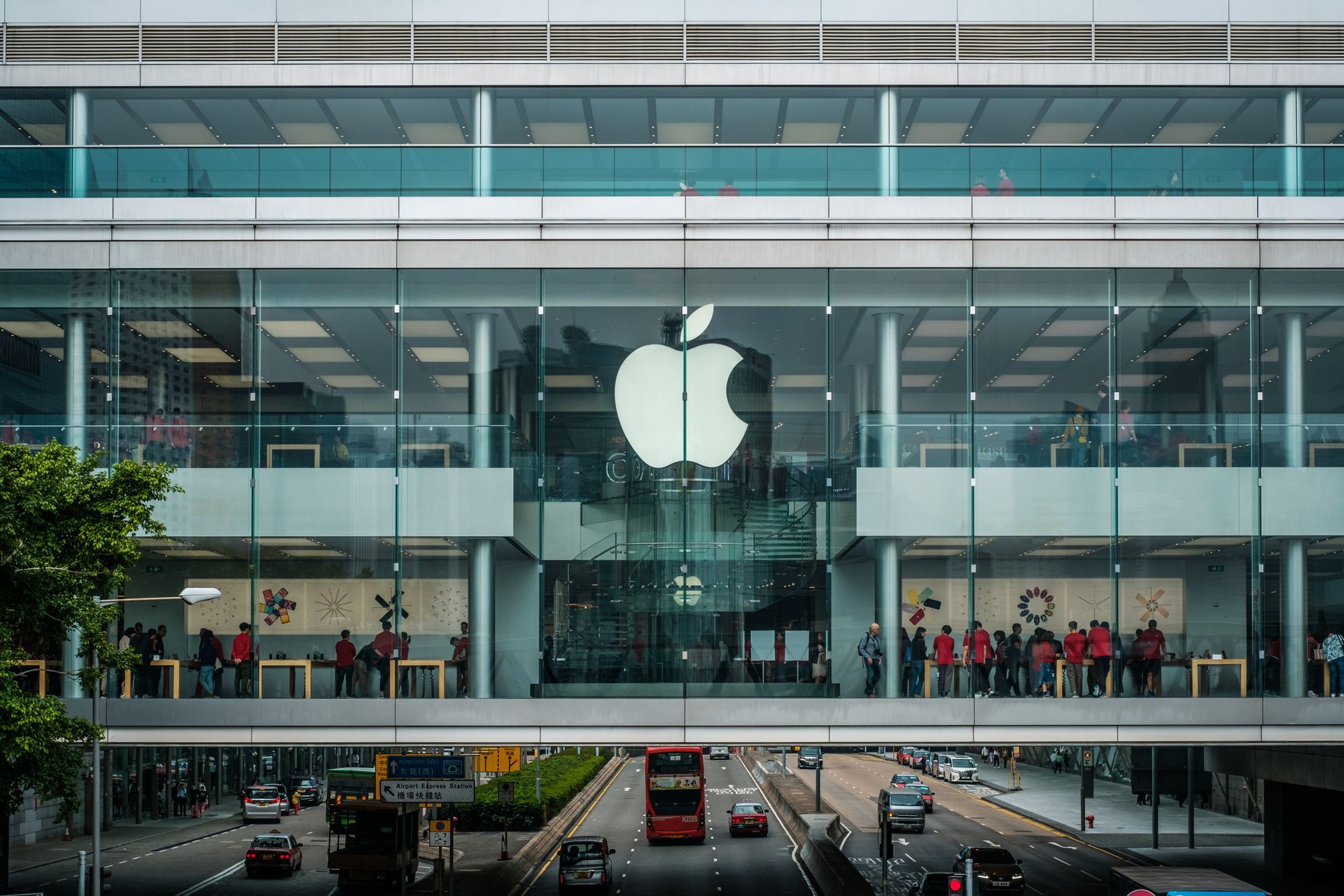 A group of people are standing on a bridge in front of an apple store.