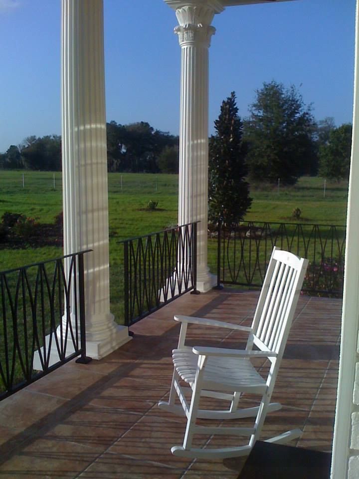 A white rocking chair sits on a porch overlooking a field
