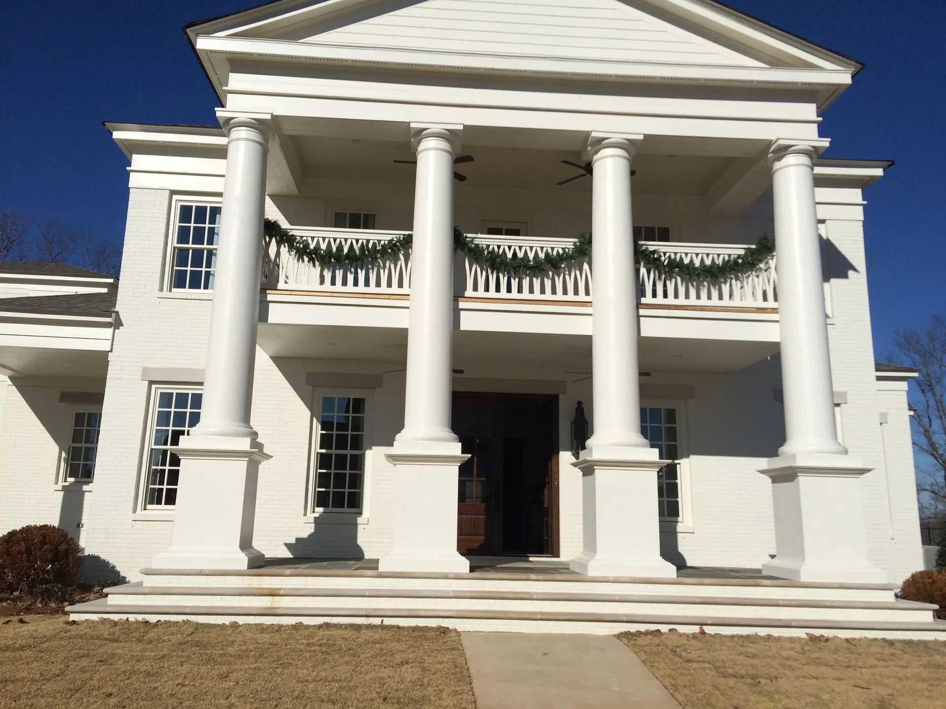 White two-story building with large columns, front porch, and a garland. Blue sky in the background.