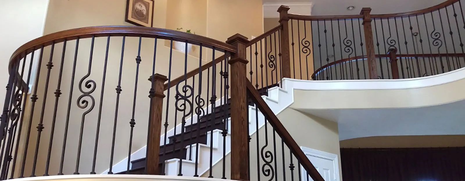 Wooden staircase with black wrought iron railing and decorative scrollwork.