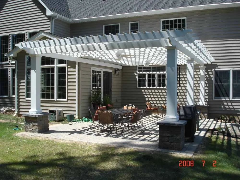 Backyard patio with a white pergola, outdoor dining table, and house exterior in sunlight