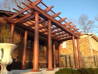 A wooden pergola is sitting in front of a brick house.