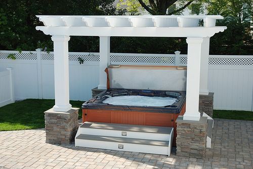 A hot tub under a white pergola in a backyard
