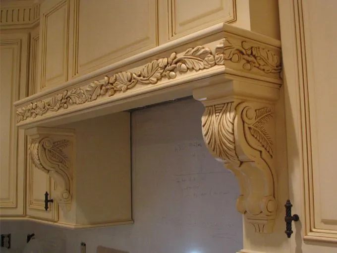 Ornate cream-colored kitchen range hood with carved floral details and decorative supports.