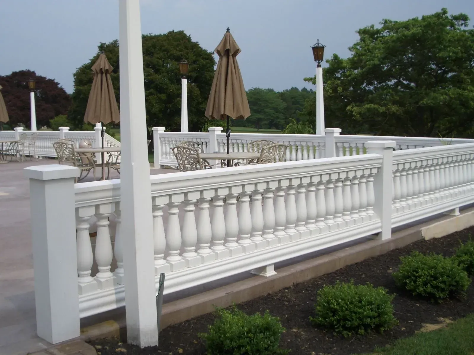 A white fence surrounds a patio with tables and chairs and umbrellas