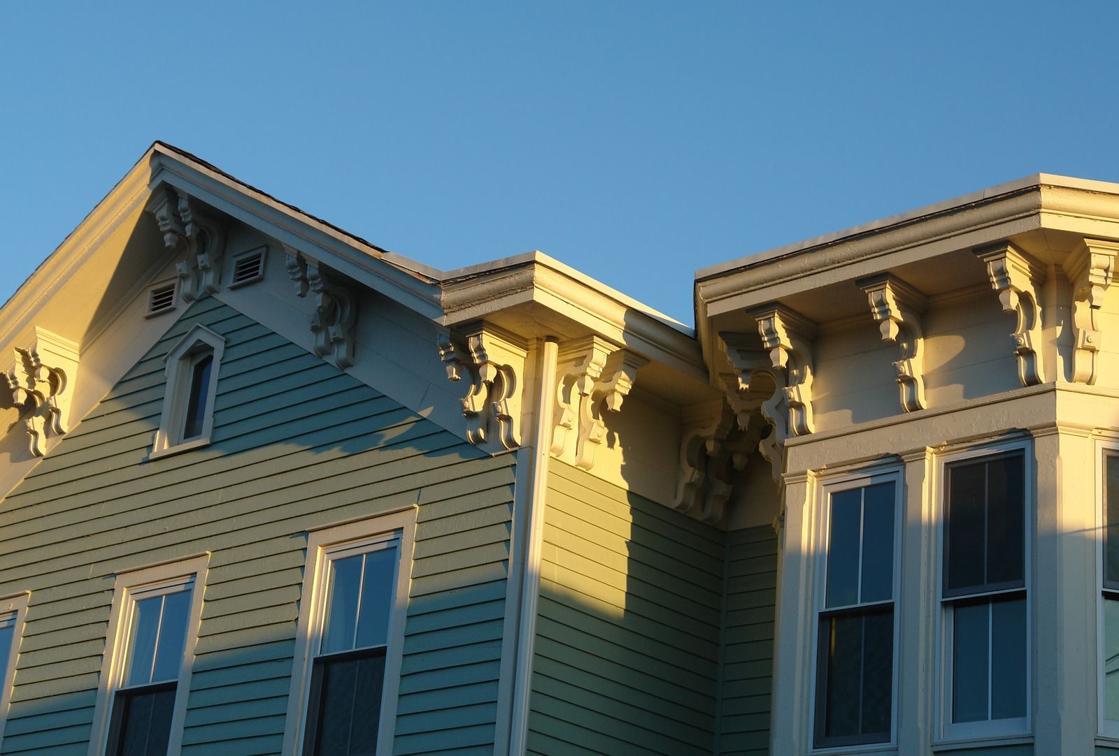 Victorian house exterior with ornate trim, in sunlight. Teal siding, yellow accents.