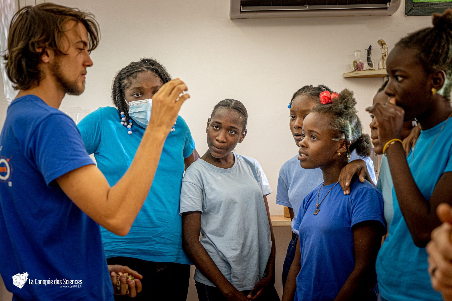Un homme en chemise bleue parle à un groupe de jeunes filles en chemise bleue.