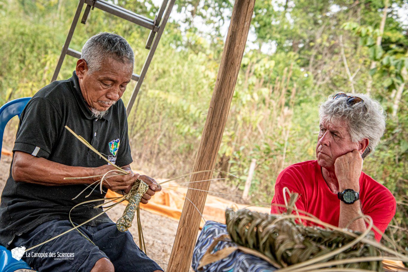 Deux hommes sont assis sous un dais et fabriquent un panier.